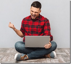 Portrait of a happy young man using laptop and celebrating success isolated over gray background
