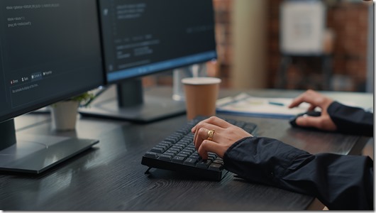 Closeup of developer hands typing code on keyboard while looking at computer screens