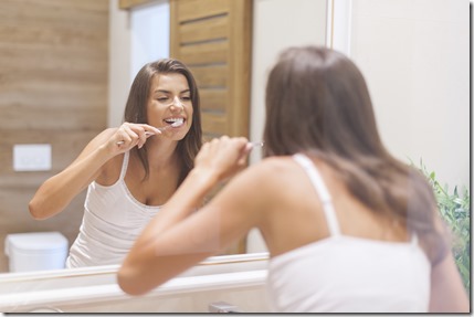 Woman brushing teeth in front of mirror. Photo taken through glass