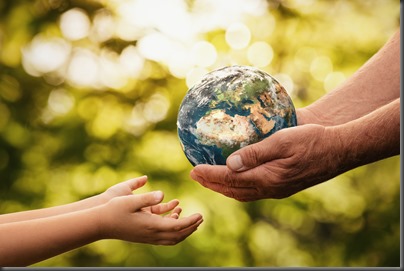 Close up of senior hands giving small planet earth to a child over defocused green background with copy space 